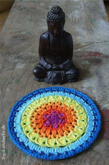 Ein Holzbuddha meditiert vor einem Mandala in Regenbogenfarben