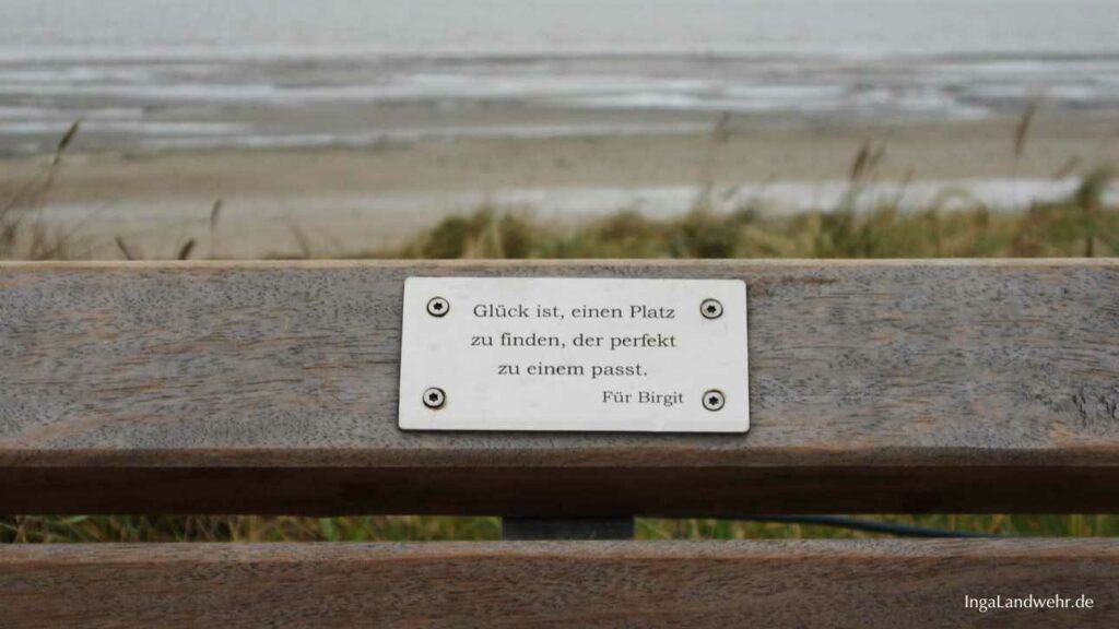 Plakette auf einer Bank mit der Gravur: "Glück ist, einen Platz zu finden, der perfekt zu einem passt." Im Hintergrund ist die Nordsee