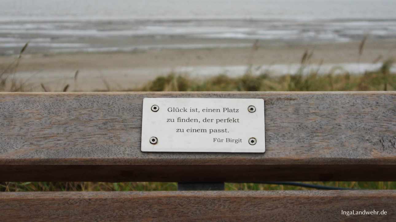 Plakette auf einer Bank mit der Gravier: "Glück ist, einen Platz zu finden, der perfekt zu einem passt." Im Hintergrund ist die Nordsee
