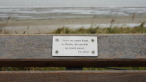 Bank am Strand. Gravur auf einer Plakette: "Glück ist, einen Platz zu finden, der perfekt zu einem passt."