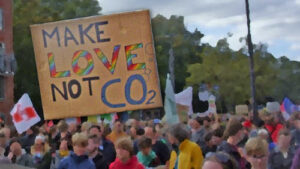 Menschen, die für Nachhaltigkeit demonstrieren. Im Vordergrund ein Schild mit der Aufschrift "Make Love not CO2"
