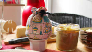 Auf einem Tisch steht ein Eierbecher mit Eierwärmer und dnaben ein Glas Quittenmarmelade.