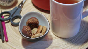 Ein kleines Schälchen mit Keksen neben einem weißen Becher mit Tee stehen auf einem Tablett