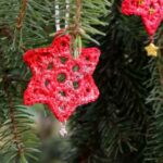Zwei rote Häkelsterne hängen in einem Weihnachtsbaum