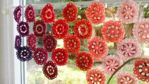 Vor einem Fenster hängt eine Scheibengardine aus viele Häkelblüten in Rottönen
