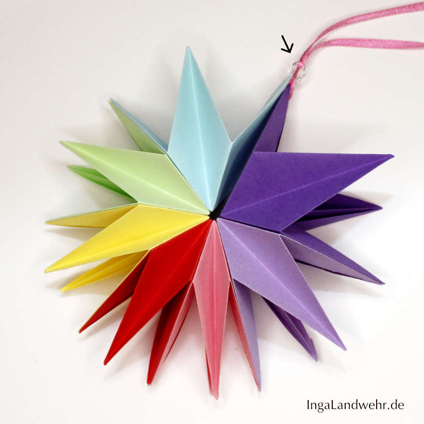 Foto für Schritt 13 der Faltanleitung für Origami-Stern: Der Origami-Stern ist auseinandergefaltet und wird der Perle zusammengehalten.